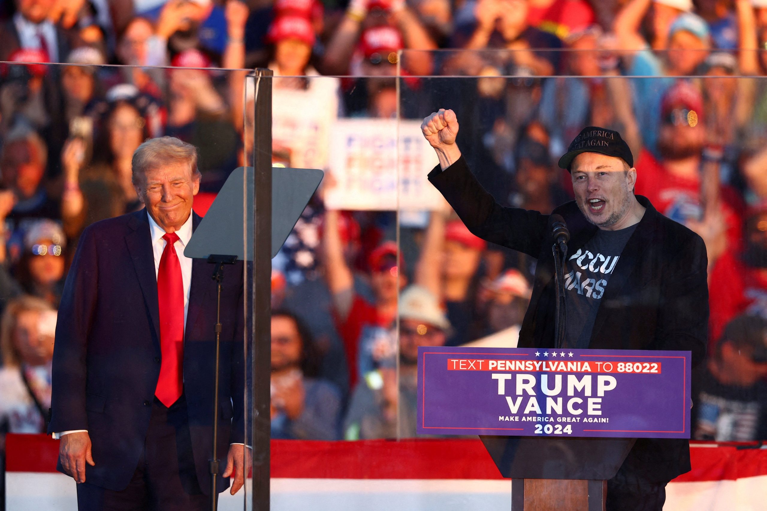 Trump and Musk at a rally being obnoxious malignant narcissists in temporary alignment. ‘Elno raises a fascist fist while wearing a black MAGA hat.